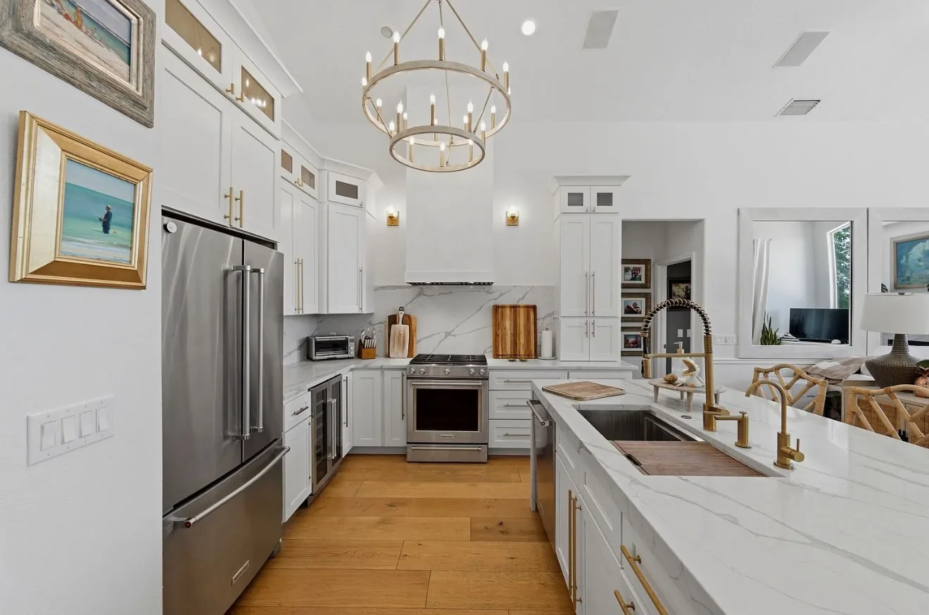 White kitchen with a waterfall marble island, brass fixtures and a ring chandelier