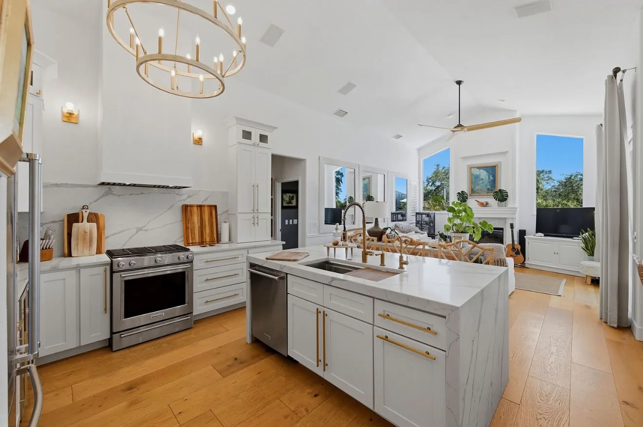 Bright white kitchen opening onto the living room, with a marble island and an oak floor